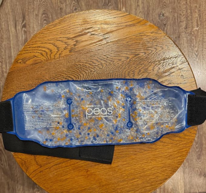 A reusable gel heating pad with a blue exterior and orange and blue beads inside, resting on a wooden table.